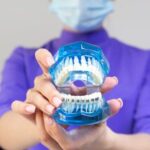 Female dentist in medical mask and protective eyeglasses demonstrating dental cleaning system with braces